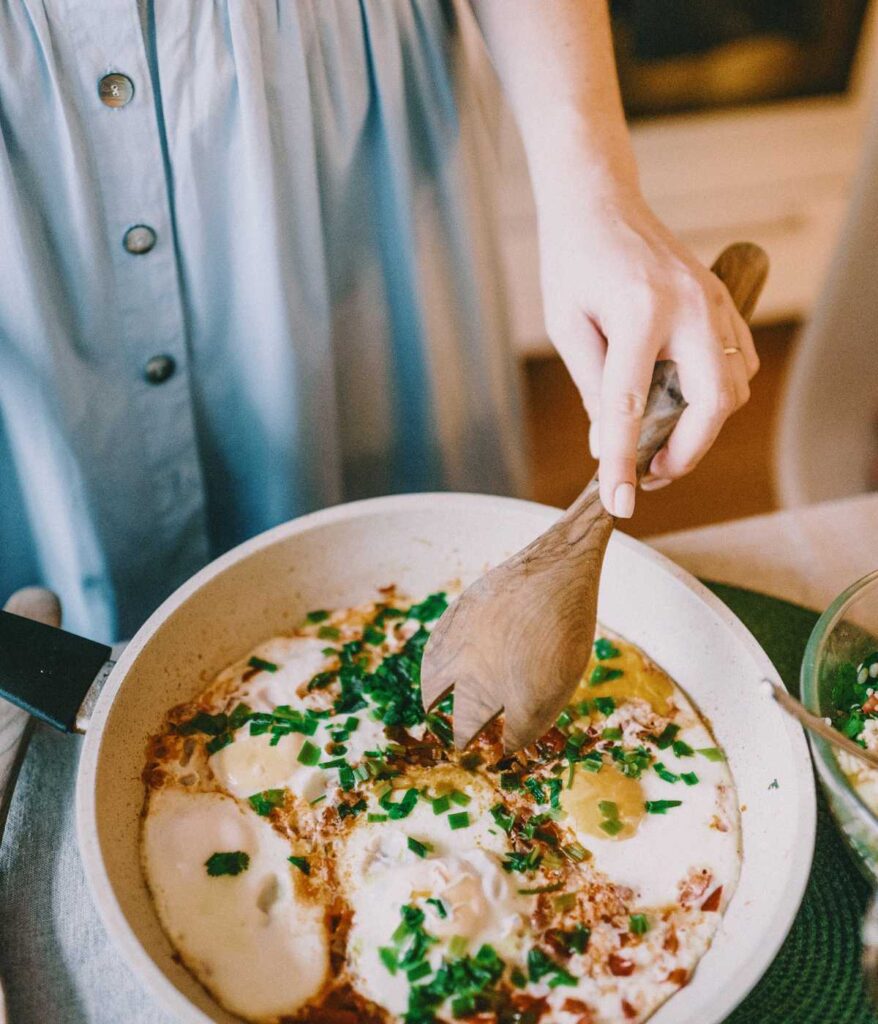 Osoba przygotowująca jajecznicę na białej patelni